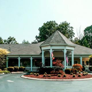 A charming building with a landscaped garden and circular driveway, surrounded by trees.