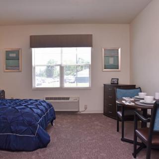 A cozy bedroom with a neatly made bed, a small table, and two chairs by the window.