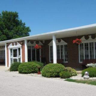 A sunny day view of a one-story brick building with columns and neatly trimmed bushes.