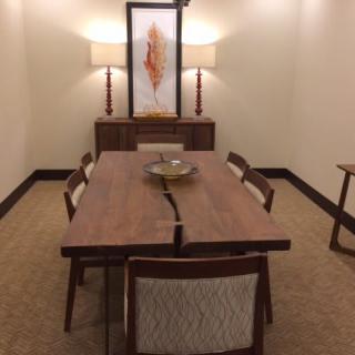 A modern dining room featuring a large wooden table with chairs, illuminated by two lamps and adorned with artwork on the wall.