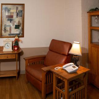 A cozy corner of a living room featuring a comfortable armchair, wooden furniture, and warm lighting.
