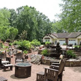 A tranquil outdoor garden with a seating area and fire pit surrounded by lush greenery.