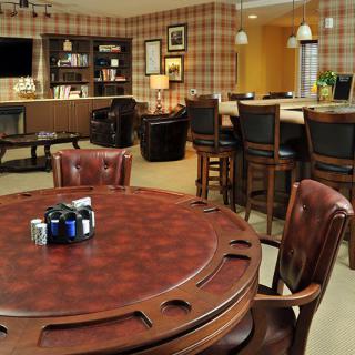 A cozy game room with a poker table and leather chairs, featuring a bar area and bookshelf.