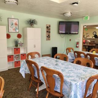 A neatly arranged dining room with a long table, wooden chairs, decorative elements on the walls, and a television mounted on the wall.