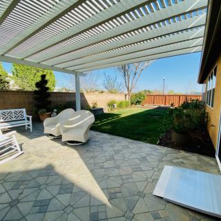 A sunny backyard patio with a pergola and outdoor seating overlooking a well-maintained lawn.