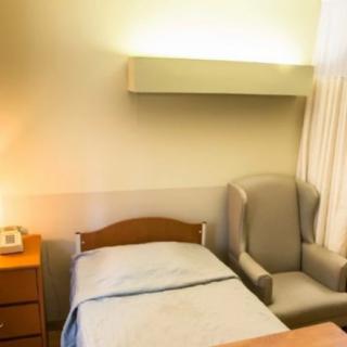 A minimalist hospital room with a single bed, armchair, and nightstand.
