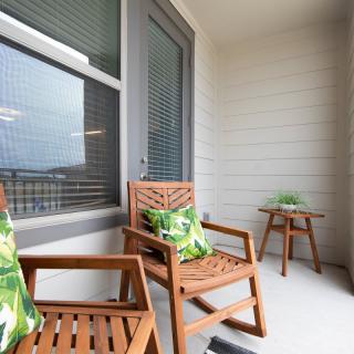 A cozy balcony setup with wooden chairs and a small table, featuring green patterned cushions and a potted plant.