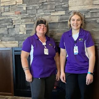 Two staff members posing together in a welcoming indoor setting.