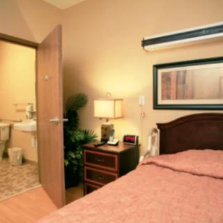A cozy bedroom with an open door leading to a bathroom, featuring a neatly made bed and a nightstand with a lamp.