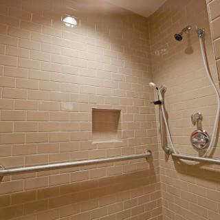 A modern shower space featuring beige tiles and accessibility grab bars.