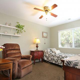 A cozy bedroom featuring a single bed, comfortable armchair, and decorative elements like plants and a ceiling fan.