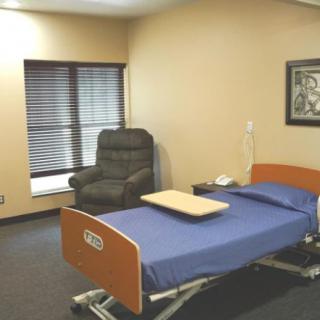 An empty hospital room with a bed and a chair next to a window.