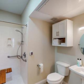 A modern bathroom featuring a shower with accessibility features, a toilet, a sink, and a storage cabinet.