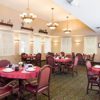 A cozy dining area featuring round tables with red tablecloths, surrounded by comfortable chairs and well-lit by elegant chandeliers.