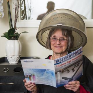 A woman sitting under a hair dryer reading a magazine in a salon.