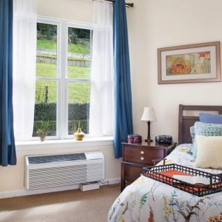 A cozy bedroom with a window view, featuring blue curtains and a neatly made bed.
