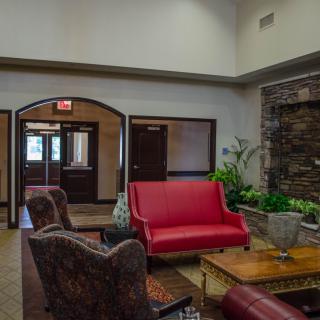A cozy lobby featuring a red couch, several armchairs, and decorative plants against a stone wall.