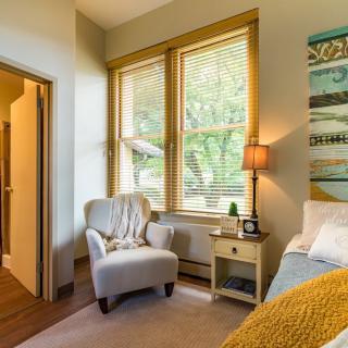 A cozy bedroom with an armchair by the window and soft lighting from a lamp.