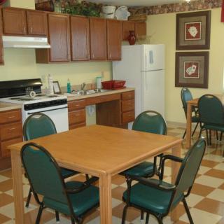 A communal kitchen and dining area featuring a table with chairs, wooden cabinets, and standard appliances including a refrigerator and stove.