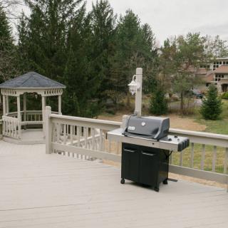 An outdoor deck with a grill and gazebo, surrounded by trees.