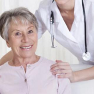 An elderly woman smiles while a nurse stands beside her, symbolizing healthcare support.