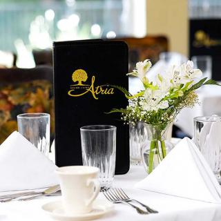 An elegantly set restaurant table with a menu and fresh flowers.