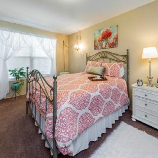 A cozy bedroom with a stylish bed adorned with pink bedding, a bedside lamp on a white nightstand, and artwork on the wall.