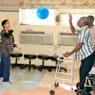 A caregiver and elderly individuals engaging in a therapeutic ball game, promoting physical activity and social interaction.