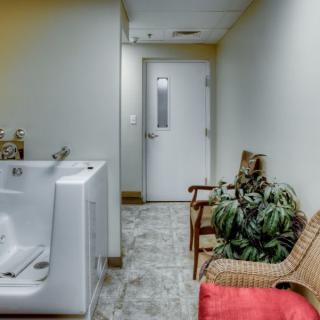 A hallway with seating, plants, a bathtub, and a door at the end.