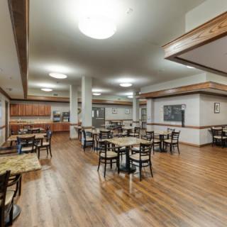 An empty restaurant dining area with wooden floors and neatly arranged tables and chairs.
