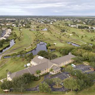 A scenic aerial view of a golf course with a clubhouse, surrounded by greenery and ponds.