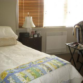 A cozy bedroom featuring a bed with a colorful quilt, a lamp on a nightstand, and a window with blinds.