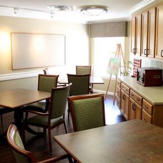 A well-lit meeting room featuring tables, chairs, a whiteboard, and wooden cabinetry.