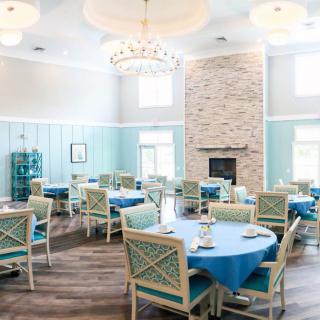 A beautifully designed dining room featuring elegant tables with blue tablecloths, comfortable chairs, a centerpiece chandelier, and a cozy fireplace.