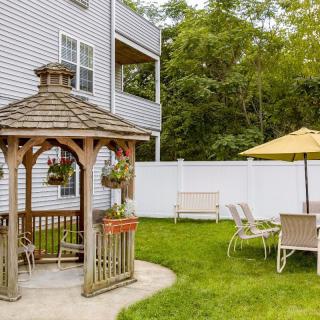 A cozy backyard with a wooden gazebo, patio furniture, and a yellow umbrella on a lush lawn.