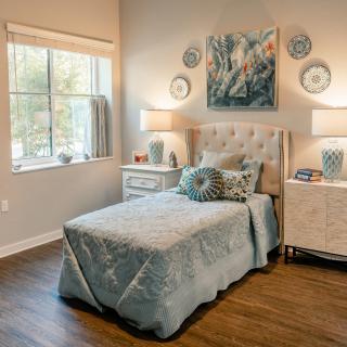 A cozy bedroom with elegant decor, featuring a bed, nightstands, lamps, and artwork on the wall.