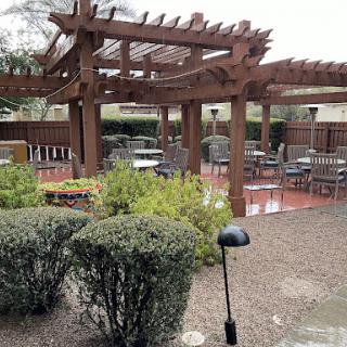 A cozy outdoor seating area featuring a wooden pergola and neatly arranged tables in a landscaped garden.