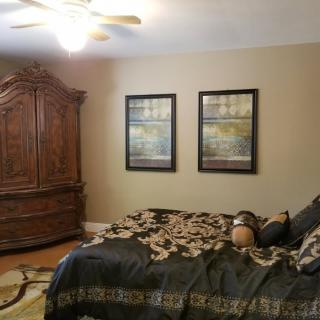 A cozy bedroom with an ornate armoire, decorative pillows, and framed artwork on the wall.