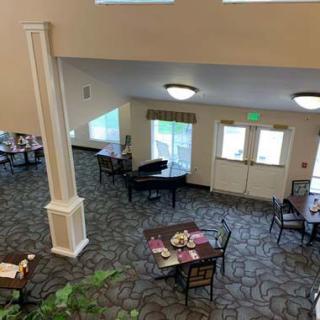 A spacious dining area with neatly arranged tables and chairs, featuring a piano and large windows.