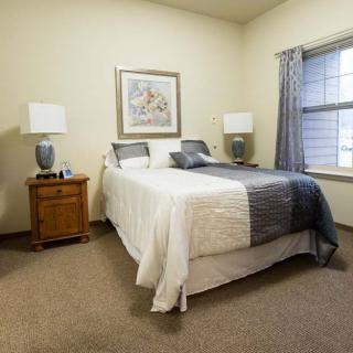 A cozy bedroom with a neatly made bed, nightstands, lamps, and a window.