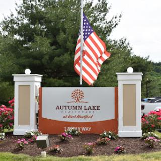 Entrance sign for Autumn Lake with an American flag and floral landscaping.