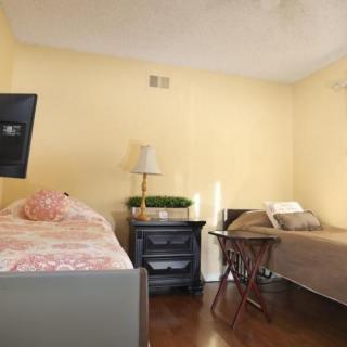 A cozy bedroom with two single beds, a nightstand with a lamp, and a wall-mounted TV.