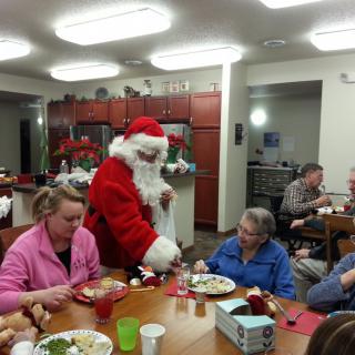 A festive gathering with Santa Claus visiting people during a holiday meal.