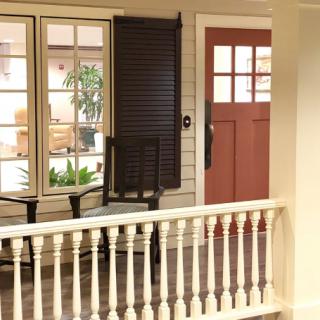 A cozy indoor porch setting with a red door, windows, and chairs next to potted plants.