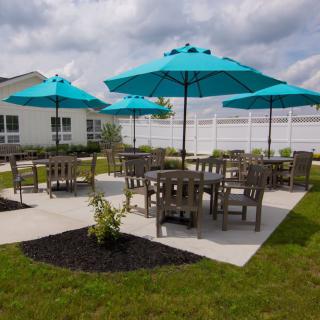 A well-maintained outdoor patio area featuring tables, chairs, and turquoise umbrellas set on a grassy lawn.
