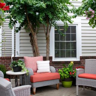 A cozy patio with wicker chairs and colorful cushions surrounded by lush greenery.