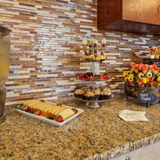 A buffet setup displaying an assortment of desserts and appetizers on a granite countertop, alongside a drinks dispenser.