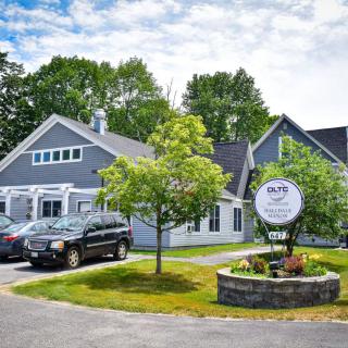 A picturesque view of a restaurant with a neatly landscaped entrance and parked cars under a cloudy sky.
