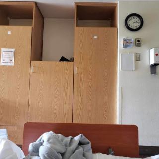 A hospital room with wooden cabinets, a wall clock, and part of a bed in view.