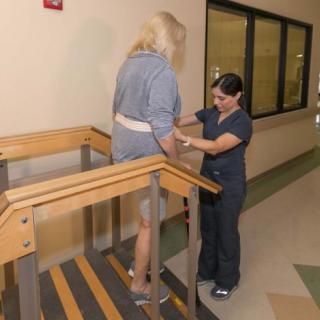A physical therapist assists a person in climbing stairs as part of a rehabilitation exercise.